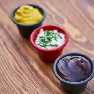 A close-up of three sauces in cups on a wooden surface, arranged in line.