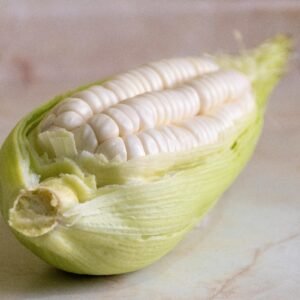 Close-up of fresh choclo corn with husk on marbled background, showcasing natural textures.