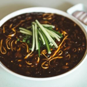 Delicious bowl of Jajangmyeon, a Korean-Chinese dish with savory black bean sauce and fresh cucumber garnishing.