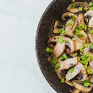 Top-down view of sautéed mushrooms and spring onions in a frying pan.