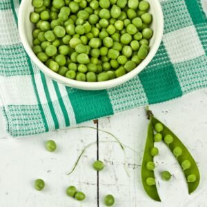 A vibrant display of green peas in a bowl with a rustic white background, ideal for food and health concepts.