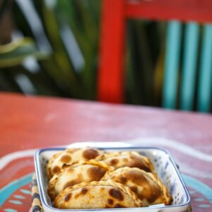 A close-up of freshly baked Argentine empanadas served on a colorful table setting in an outdoor setting.